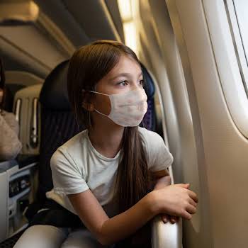 Happy girl traveling by plane wearing a facemask