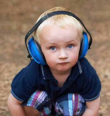 Shot of a little boy sitting and looking up at the camera with protective headphones over his ears at a music festival