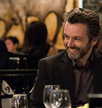 Michael Sheen sitting at a table and smiling