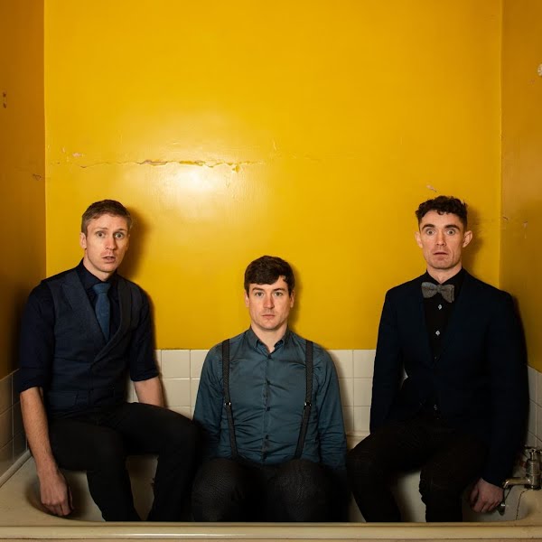 three men standing together in front of a yellow wall