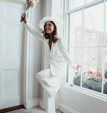 woman in a white suit and hat holding a bouquet of flowers